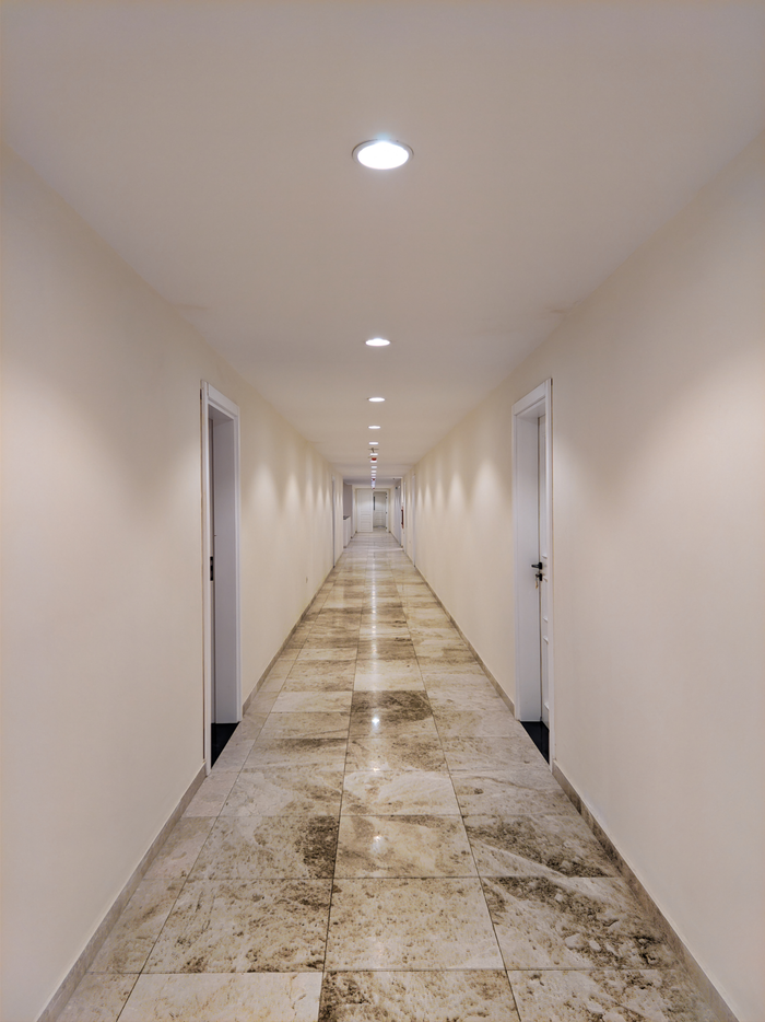 Long marble hallway featuring white doors and modern lighting, conveying luxury and elegance.